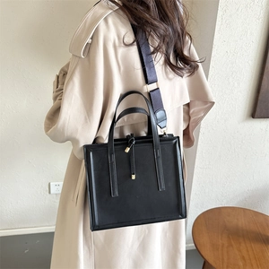 Close-up of black PU handbag featuring gold metal knot detail and wide fabric strap