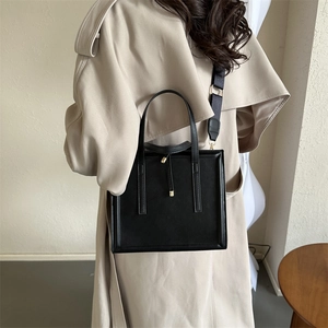 Detail of black matte PU leather bag featuring gold drawstring and wide strap on model