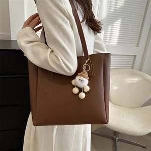 Deep brown PU leather tote bag with white plush doll charm shown on model in studio