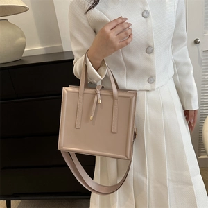 Chic beige structured handbag with gold accents shown being held by a model in a studio