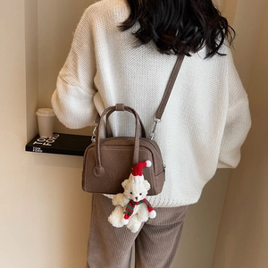 Detail of dark brown leather crossbody bag with a cute white teddy bear charm and soft strap