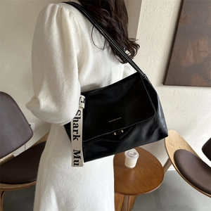 Detailed side view of black PU leather shoulder bag with a logo strap on a model