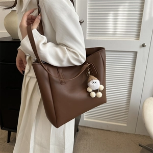 Detail of a dark brown PU leather tote bag with a cute white plush monster charm