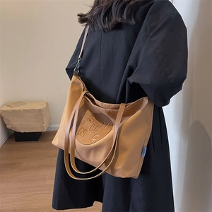 Close-up of caramel canvas tote bag with brown leather straps and embossed round logo
