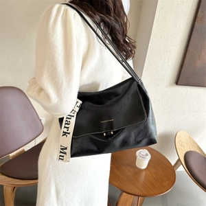 Detail of black PU leather shoulder bag featuring wide fabric strap with text and gold logo