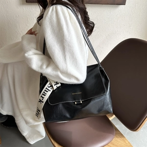 Detail of black PU shoulder bag with stylish wide fabric strap and golden logo text