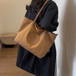 Detailed side view of a large caramel canvas tote bag with SHUNO patch on black attire