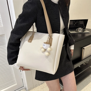 Chic white leather tote bag with brown straps and plush charm shown in office setting