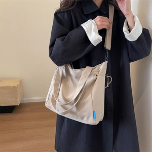 Detail of beige canvas tote bag with adjustable shoulder strap worn by a model