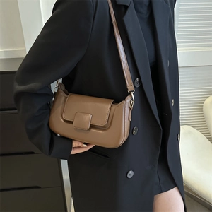 Brown leather crossbody bag detail on model wearing a black suit in a minimalist setting
