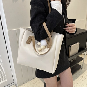 Minimalist cream tote bag with brown leather handles and a plush pompom accessory