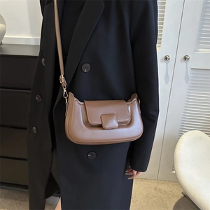 Detail of a brown leather crossbody bag with square buckle on a black coat outfit