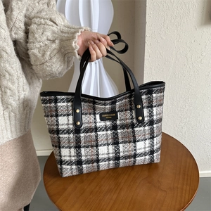 Close-up of winter wool plaid tote bag with golden rivets and black leather handles