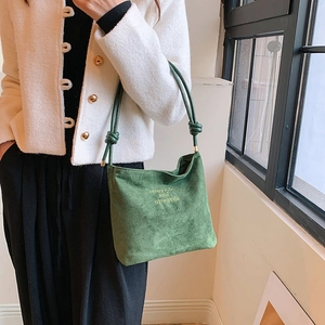 Close-up of green suede shoulder bag with onwards and upwards embroidery and knot strap