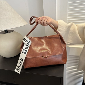 Detailed view of brown PU leather shoulder bag with gold metal buckle and lettered strap