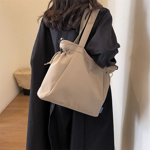Detail view of beige canvas tote bag with adjustable drawstring and side brand label
