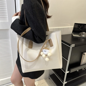 Close-up of cream white PU leather tote bag with brown handle and plush eye pendant