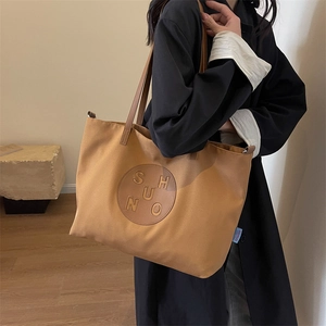 Close-up of brown canvas tote bag featuring circular leather patch and brand logo detail
