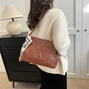 Detail of a brown PU leather crossbody bag with wide jacquard strap and gold hardware