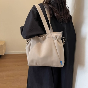 Detail of beige canvas tote bag with drawstring closure and blue woven label on model