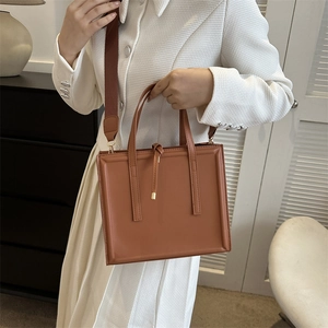 Detail of a brown PU leather tote bag with sturdy dual handles and a wide shoulder strap