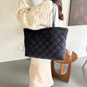 Gros plan sur un sac cabas noir matelassé avec surpiqûres en losanges et anses en cuir