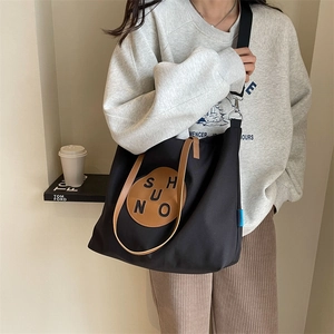 Minimalist black canvas tote bag with brown leather straps and adjustable crossbody strap
