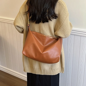 Detail view of brown lychee-textured leather hobo bag worn over a beige sweater