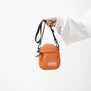 Orange corduroy mini crossbody bag with Fashion label and black adjustable nylon strap