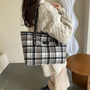 Detail view of plaid tote bag with wool texture, leather handles and metallic brand tag