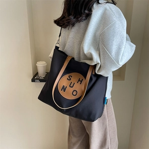 Detailed back view of a black canvas tote bag with brown leather straps and brand patch
