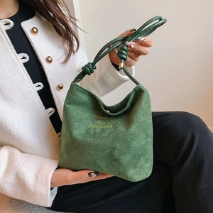 Detail of green faux suede handbag featuring yellow embroidery and knotted handle strap