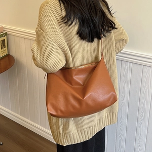 Lifestyle shot of a brown pebbled leather hobo bag worn with a beige knitted sweater