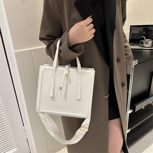 Close-up of a white rectangular PU leather handbag with wide fabric strap and tassel detail