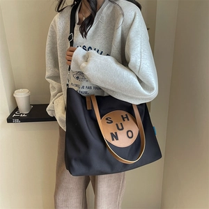 Detail of minimalist black canvas tote bag with brown leather handles worn by model
