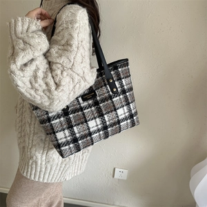 Close-up of winter plaid tote bag featuring black leather handles and gold rivet accents