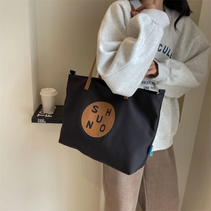 Detail of black canvas tote bag with brown leather circular logo and slim handles