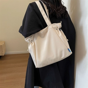 Detail of off-white canvas tote bag with black drawstring and red-blue brand label