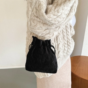Close-up of black corduroy drawstring crossbody bag with woven strap and ruffle edge