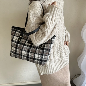 Detail of tweed tote bag with black leather strap and metallic gold rivet accents