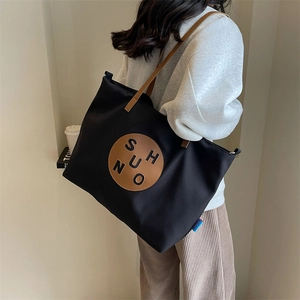 Detail of black canvas tote bag with brown leather patch and woven label on shoulder strap