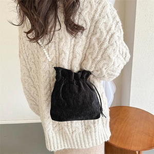 Detail of black corduroy bucket bag with elegant white pearl chain and drawstring closure
