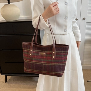 Detail of classic plaid tote bag with dark brown leather straps and branded metal plaque