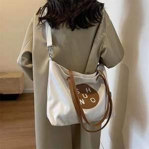 Detailed view of the large white canvas tote bag worn with a long strap over a trench coat