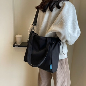Detail of black nylon tote bag with adjustable strap and side drawstring on model