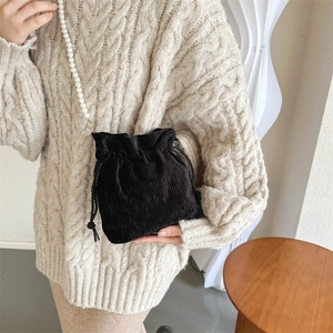 Detail of black corduroy bucket bag with pearl strap and drawstring on a beige sweater