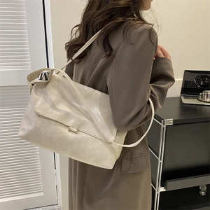 Detail of creamy white large shoulder bag with wide letter M strap on a model