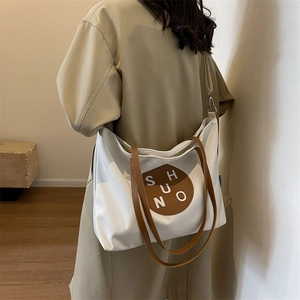 Close-up of a white canvas tote bag with brown leather handles and adjustable shoulder strap