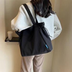 Detail of black nylon drawstring tote bag with wide shoulder strap worn by a model