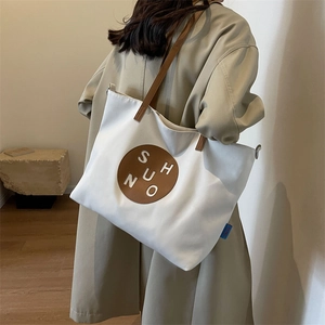 Detail of high-capacity canvas crossbody bag showing side view on a model in beige